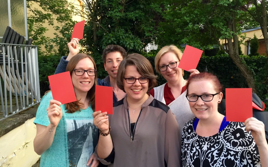 Der Vorstand der AIDS-Hilfe hält rote Karten in die Kamera - eine Aktion zum IDAHOT
